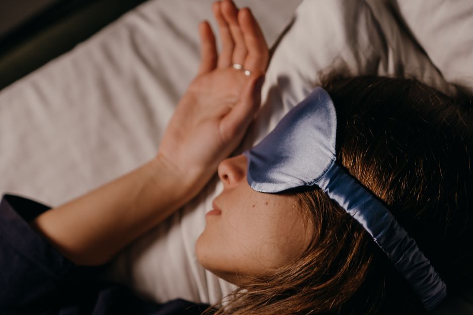 A person resting in bed with a blue sleep mask over their eyes