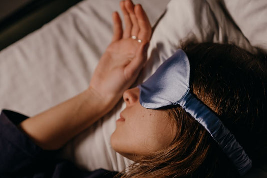 A person resting in bed with a blue sleep mask over their eyes