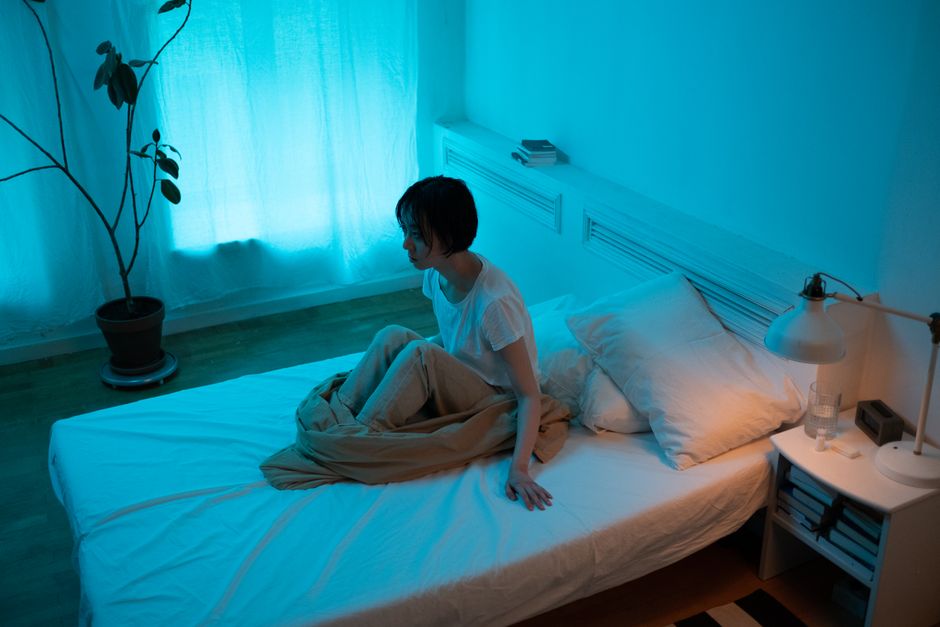 Woman sitting on a bed in a dimly lit bedroom at night